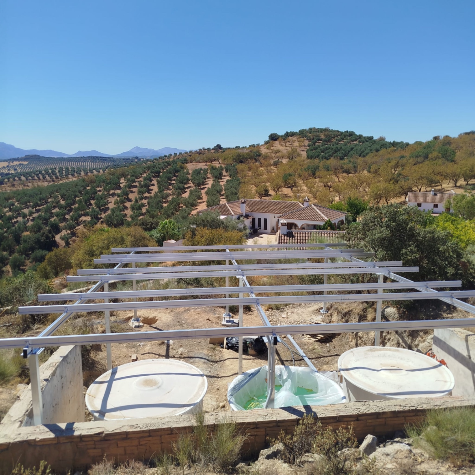 Ground-mounted solar frame in front of the finca in Loja, with water tanks in the concrete pit