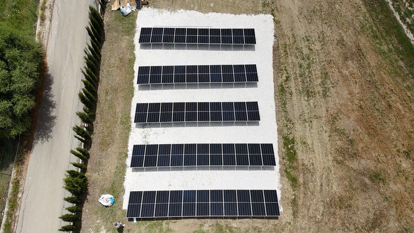 Aerial top-down view of 52-panel JA Solar ground-mount array on white gravel base, Coín